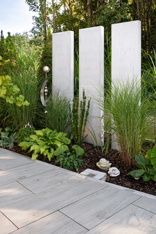 Three steles as privacy screens made of high-performance concrete in a landscaped garden section.