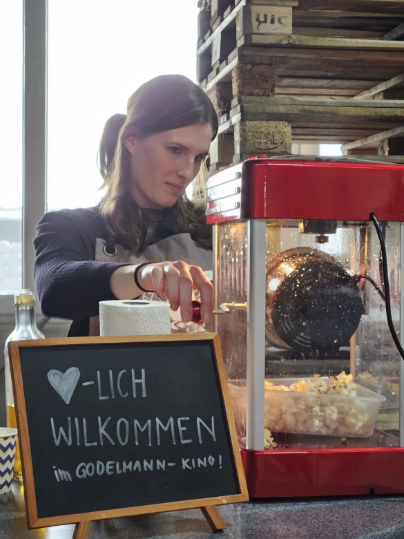 GODELMANN Kino: an einer Popcornmaschine steht eine junge GODELMANN Mitarbeiterin.