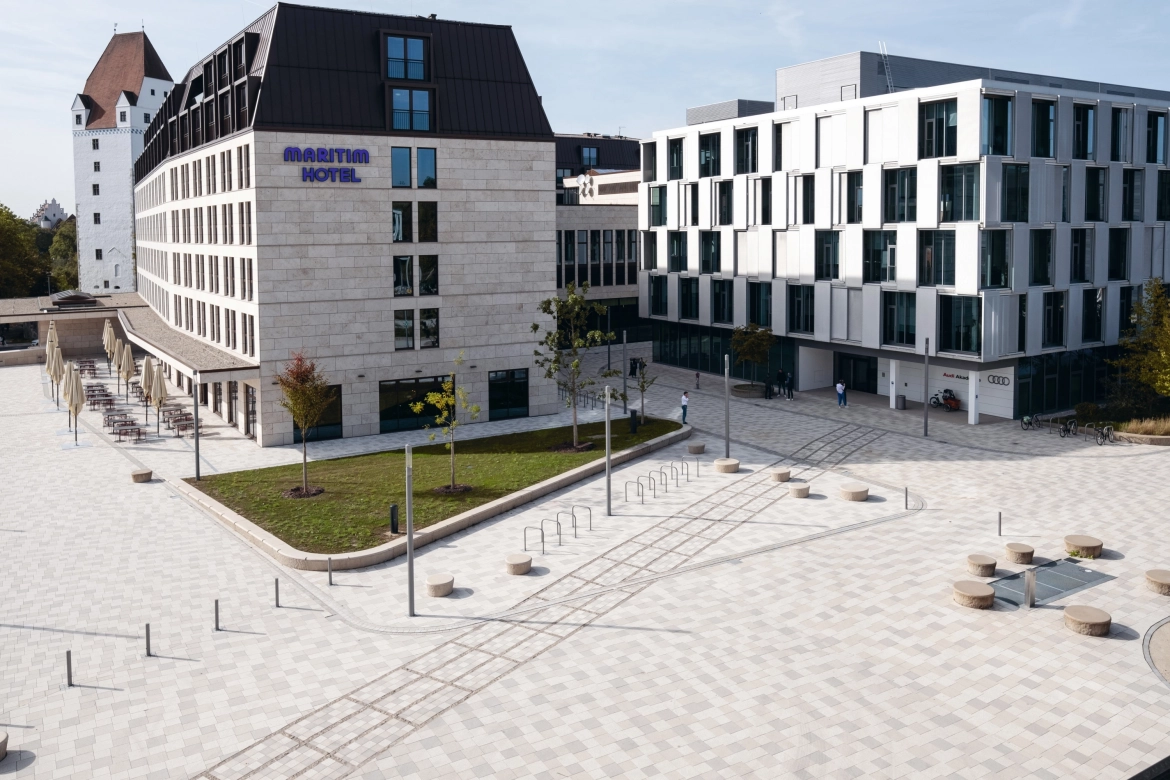 Stadtplatz vor einem Hotel mit farblich abgestimmten, wild verlegten Pflastersteinen in Grautönen.