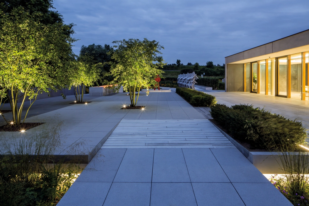Evening atmosphere in the idea garden. Trees break through the straight-lined terrace.