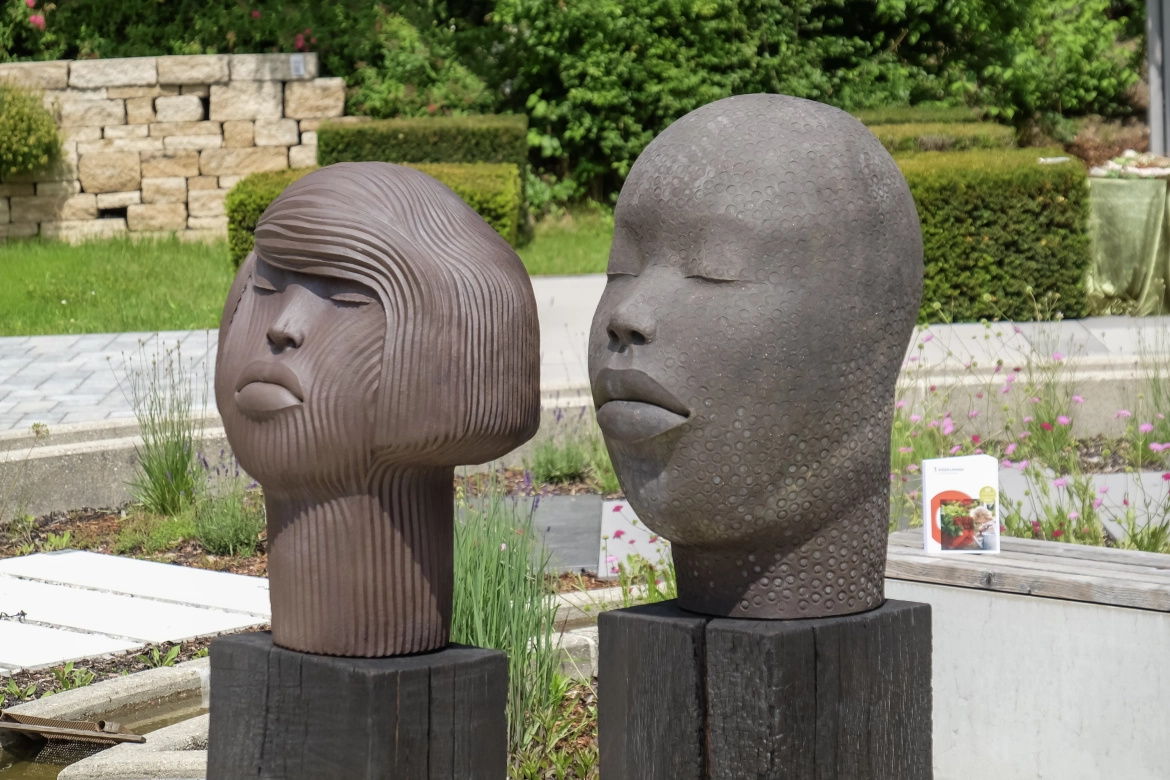 Große Tonskulpturen, darunter charakteristische Köpfe und eine Frauenfigur von Frauke Meszaros, sind im Ideen-Garten ausgestellt und ziehen die Aufmerksamkeit der Besucher auf sich.