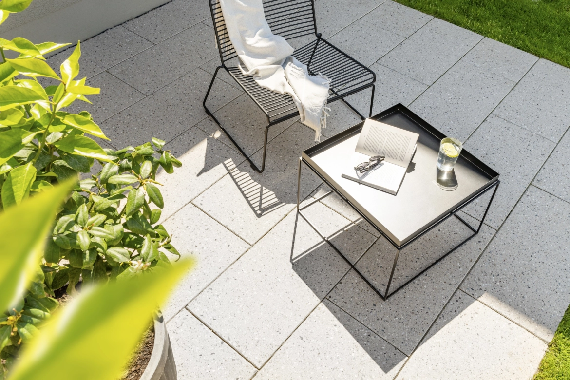 Terrasse mit feinen Terrassenplatten in beige hell und einem schwarzen Metallstuhl und Tisch 
