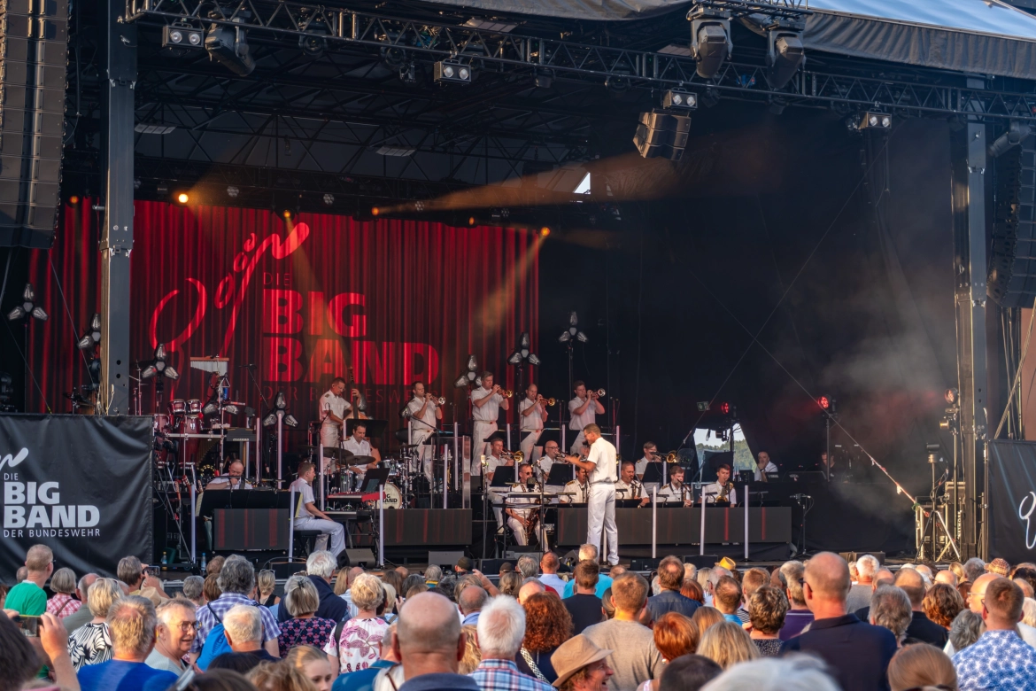 Die BigBand der Bundeswehr auf der Bühne: Die Musiker tragen weiße Kleidung und sind auf ihre Musik fokussiert.