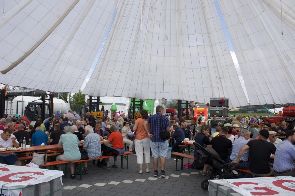 Unter einer luftigen Zeltkuppel genießen Besucher kulinarische Köstlichkeiten wie Fischburger, Bratwurstsemmeln, Pizzazungen und Kuchen inmitten von Blumen und Pflanzen.