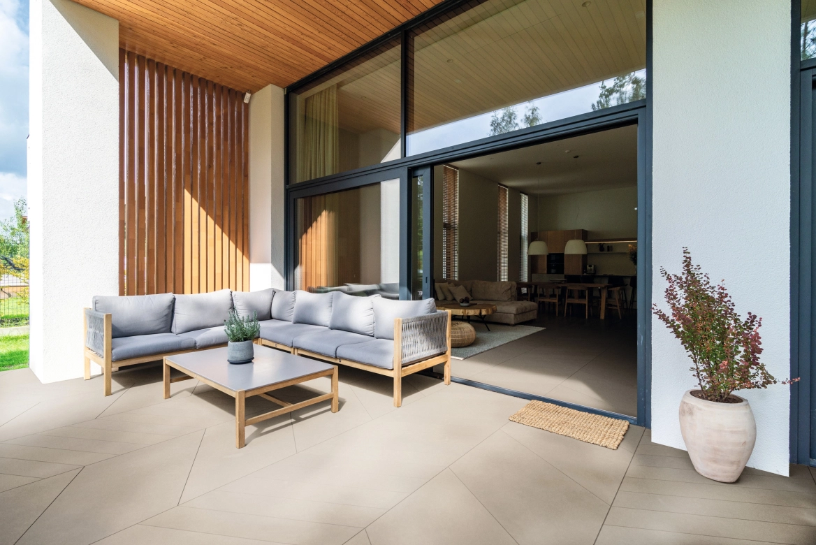 Terrace with outdoor couch and view into the living room. Terrace and living room were covered with AWA tile, creating a smooth transition between inside and outside.