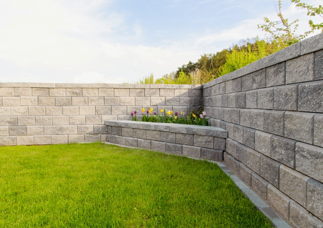 hohe Gartenmauer GDM.Allan block in grau mit Abdeckstein und dreieckigem Hochbeet in der Ecke der Mauer 