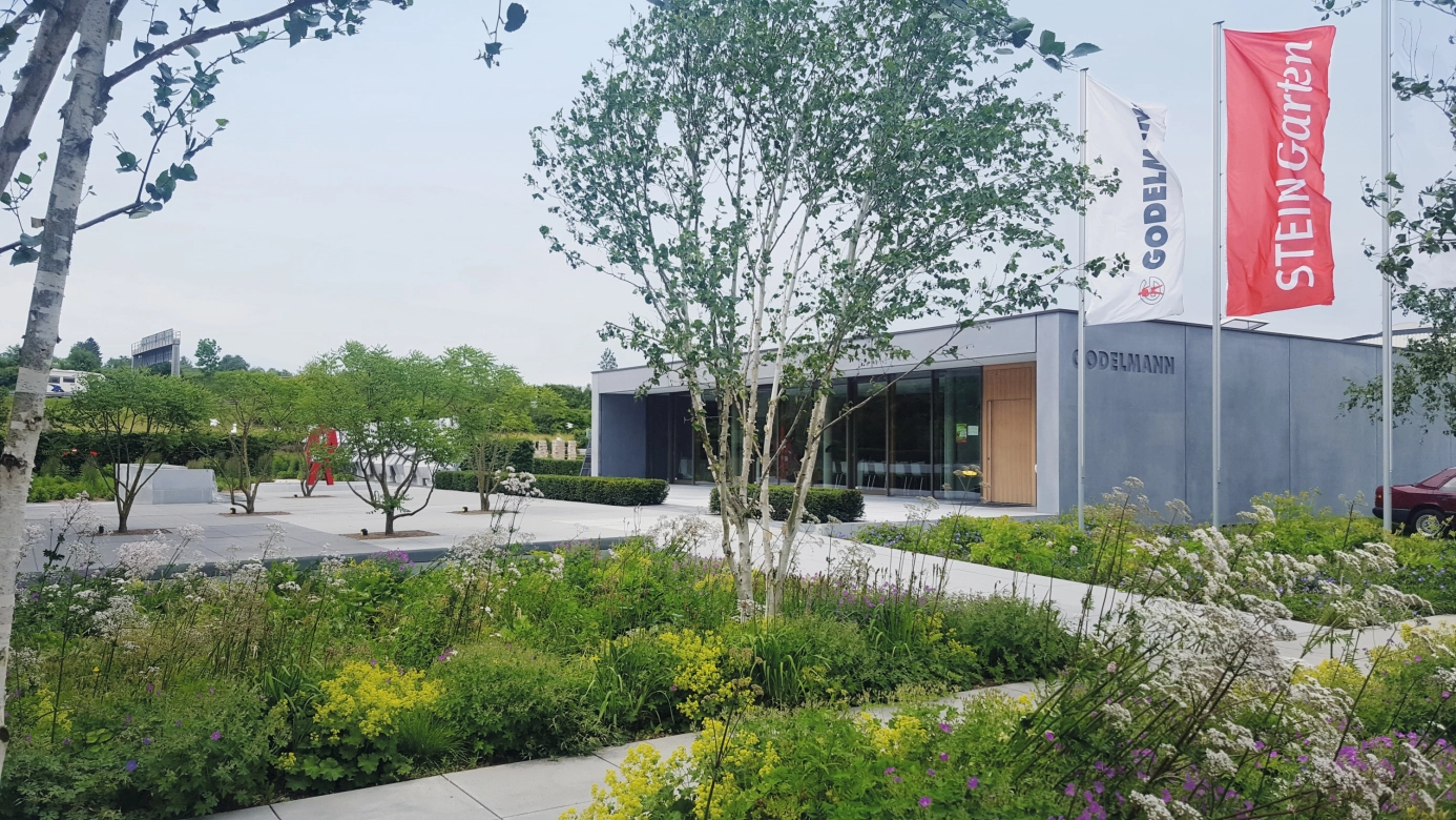 Modern idea garden with many plants and trees. The garden transitions over a plaza into a modern office building.