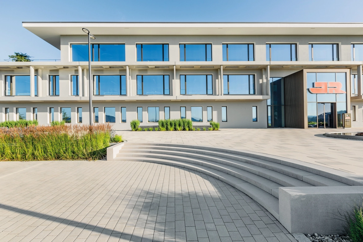gerundet verlaufende Stufenanlage in grau mit passenden Pflastersteinen im Reihenverband  vor einer Unternehmszentrale.
