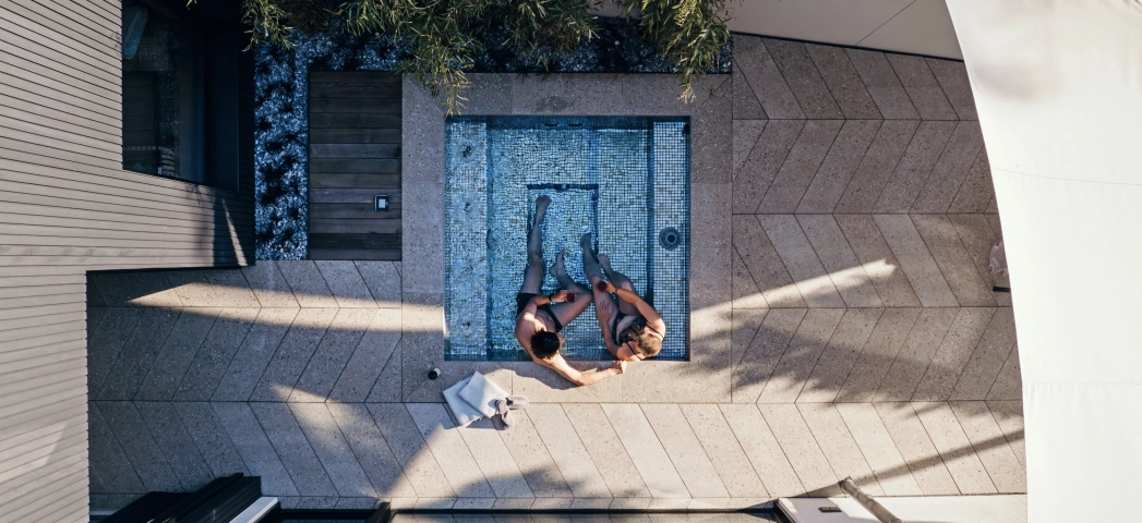 kleiner Whirlpool Jacuzzi im Außenbereich, umgeben von Betonfliesen in Fischgrät-Optik, Terrazzo mit dem Unterton Sand-Grau, und Pool-Einfassung aus Beton