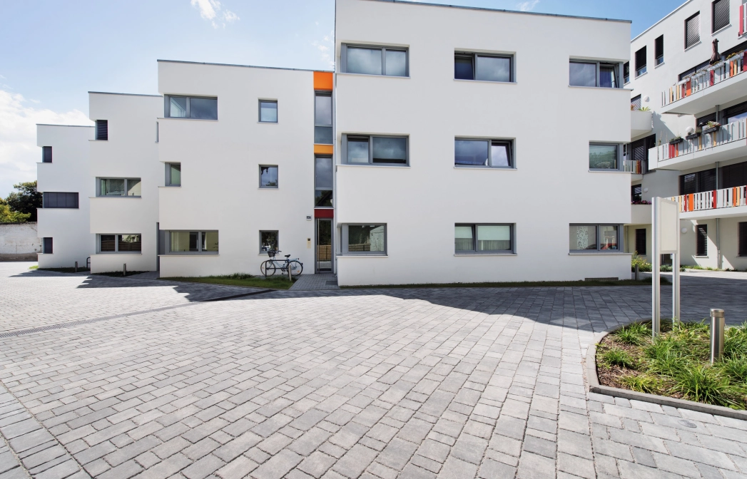 breite hellgrau gepflasterte Hofeinfahrt zu mehreren Wohngebäuden mit weißer Fassade