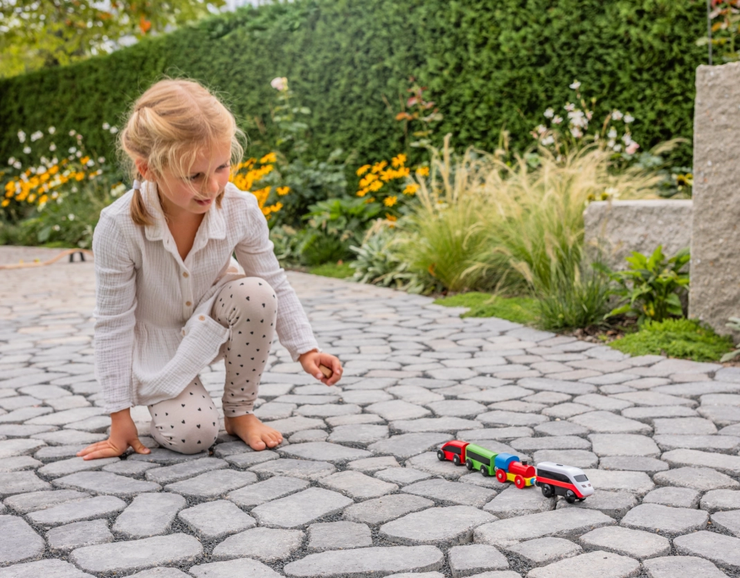 Mädchen spielt mit Spielzeugzug auf Gehweg aus Kleinpflastersystem GDM.Bolero stone in grau