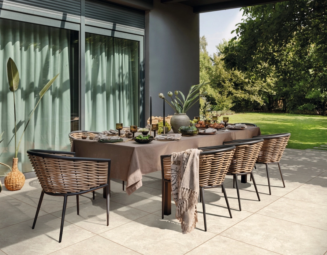 Terrasse mit großen Keramikplatten GDM.Liva twice in Kalkstein hell auf der eine üppig gedeckter Tisch und Stühle stehen