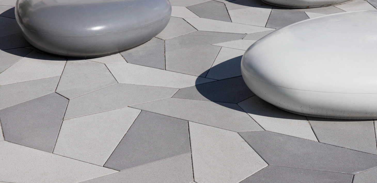 kieselförmige Sitzbänk aus Sichtbeton und polygonale Pflasterplatten in verschiedenen Grautönen