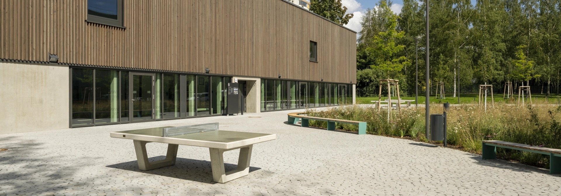 Vorplatz der Grundschule mit natürlichem Ökopflaster GDM.BOLERO stone auf dem eine Tischtennisplatte steht. Im Hintergrund eine natürliche Wiese und ein Wald.