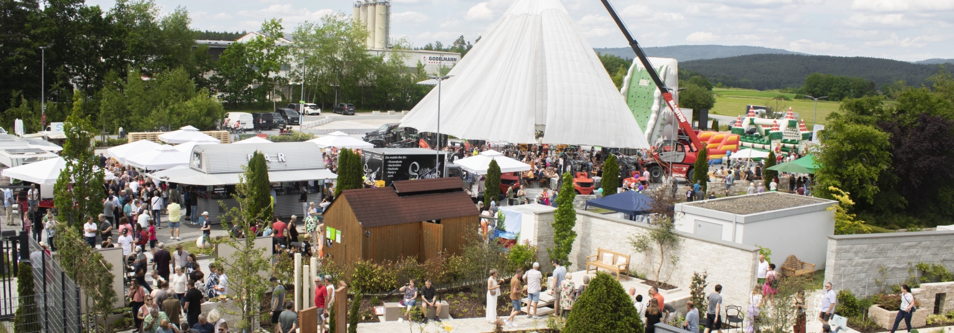 Eine Luftaufnahme zeigt das weitläufige Gelände des „Tag des Gartens“ mit zahlreichen weißen Zelten, Ausstellungsständen und einer großen Besucherzahl, umgeben von grüner Landschaft.