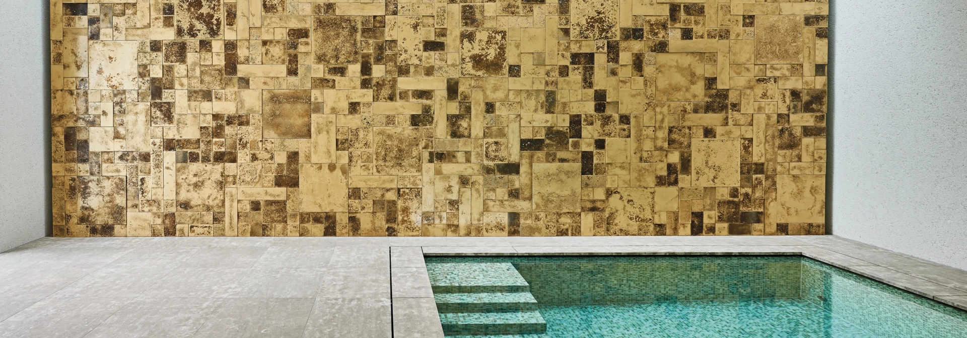 Indoor-Pool vor einer Wand aus Gold- und Bronzefarbenen Wandfliesen