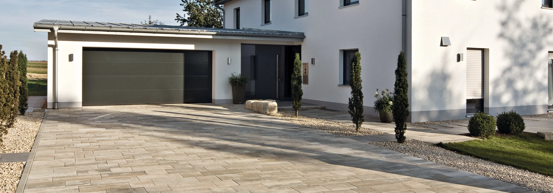 Driveway of a detached house with garage and plants on a private property.