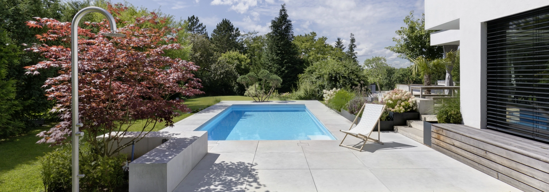 Landscaped garden with pool and large-format patio slabs on a private property.
