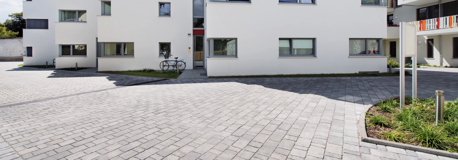 breite hellgrau gepflasterte Hofeinfahrt zu mehreren Wohngebäuden mit weißer Fassade