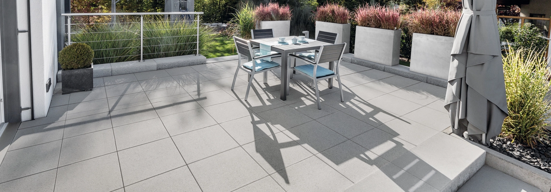 Large terrace with gray patio slabs and steps surrounded by planters.