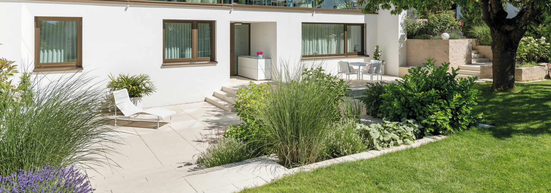 Private modern garden with sandstone-colored terrace and lots of greenery