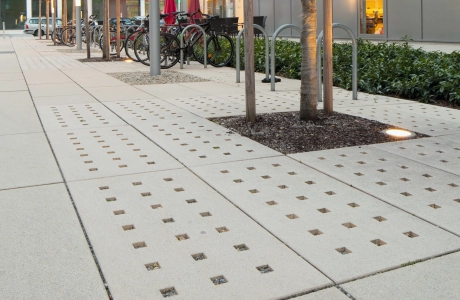 Baumscheiben aus Steinplatten neben Fahrradständer auf begrüntem Innenhof