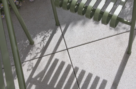 Nahaufnahme von grauen Terrassenplatten aus Beton. Darauf stehen dunkelgrüne Sitzmöbel.