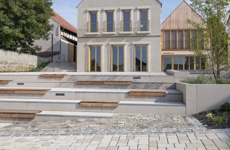 Modern house with pitched roof next to an older building, with an ecological surface covering in the foreground.