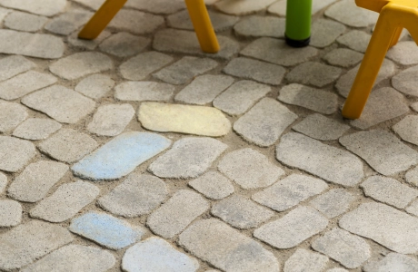 Zwei gelbe Kinderstühle und ein grüner Tisch auf GDM.BOLERO, auf dem Tisch liegen drei bunt bemalte Steine.