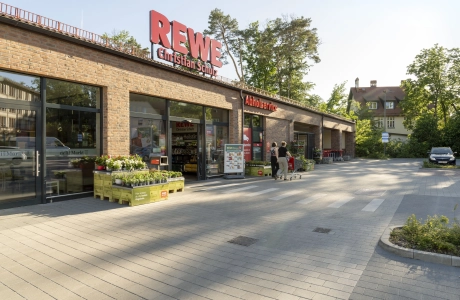 GDM.KLIMASTEIN aBG vor dem Eingangsbereich des REWE Markts Christian Schulz mit Zebrastreifen und Backsteinfassade.