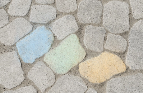 Drei mit blauer, grüner und gelber Kreide bemalte Pflastersteine auf einer Fläche aus GDM.BOLERO.