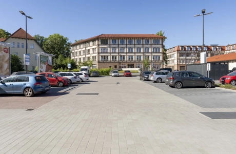 Parkplatz mit Stellflächen und Fahrgassen aus GDM.KLIMASTEIN aBG, umgeben von Gebäuden, Leuchten und abgestellten Fahrzeugen.
