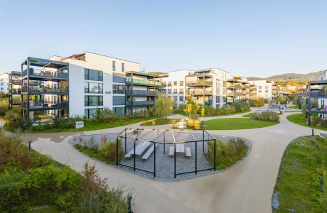 Weitläufige Wohnanlage mit modernen Wohnhäusern und angelegtem Park mit Rasenfläche und Sitzgelegenheiten