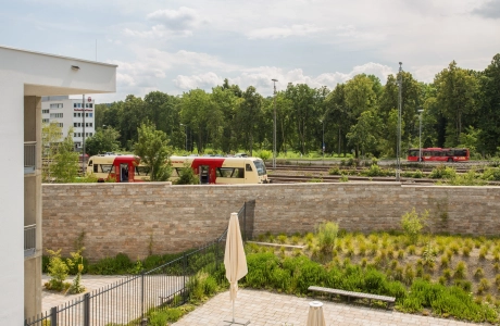 helle sandfarbene Schallschutzwand in einem begrünten Garten mit dahinter liegenden Schienenverkehr