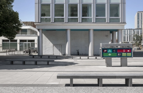 Eingang zu Hochhaus mit grau gepflastertem Platz und Sitzbänken