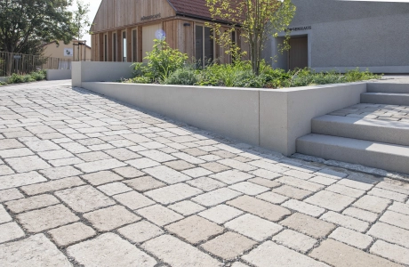 Ecologically paved area with interlocking stones leading to concrete steps and a raised bed next to a building.