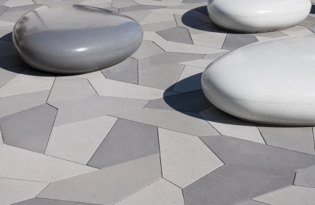 kieselförmige Sitzbänk aus Sichtbeton und polygonale Pflasterplatten in verschiedenen Grautönen