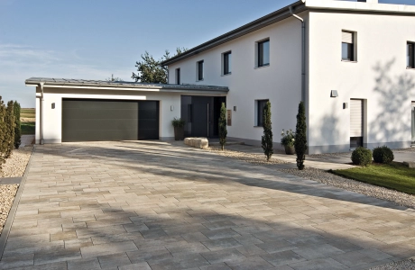 Driveway of a detached house with garage and plants on a private property.