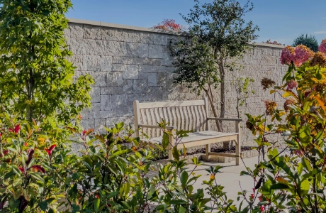 Wooden bench in front of a wall as a privacy screen in a landscaped garden.