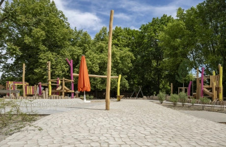 Spielbereich der Kita Wolkenschaf mit Naturholz-Spielgeräten, farbigen Pfosten und geschlossenem orangefarbenem Sonnenschirm auf GDM.BOLERO.