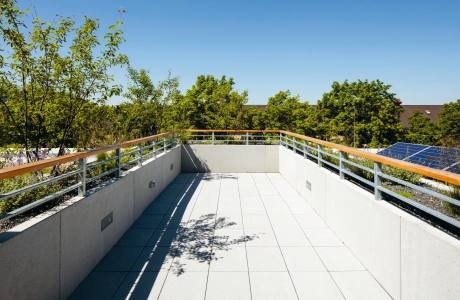 Dachterrasse aus hellen Pflastersteinen und Betonumrandung mit Eisen- und Holzgeländer mit Blick auf Bäume 