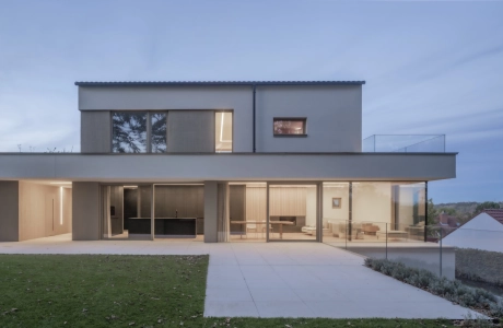Abendliche Aufnahme eines hell beleuchteten, modernen Wohnhauses. Im Vordergrund ist ein gepflegter Rasen und eine große Terrasse zu erkennen.