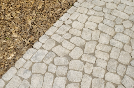 Mit GDM.BOLERO gepflasterter Weg, angrenzend an eine Fläche mit Rindenmulch.