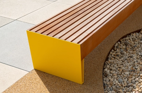 Gelbe Sitzbank mit Holzauflage neben einer Fläche aus GDM.SCENIC individual und einem Kiesbeet.