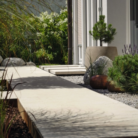 Sandstone-colored path around the house with large format and greenery.