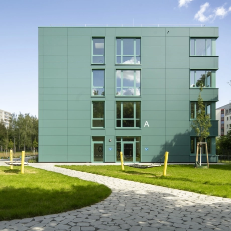 Vorplatz Schulgebäude mit grünen Flächen und Gehweg mit Pflasterung: der Flächenbelag GDM.BOLERO stone ist versickerungsfähig, begrünbar und durch seine organische runde Form besonders in der Flächengestaltung