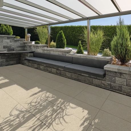 Terrasse mit GDM.Liva light Keramikverbundplatten in Kalkstein hell und einer abgestuften Gartenmauer inklusive integrierter Sitzmöglichkeit