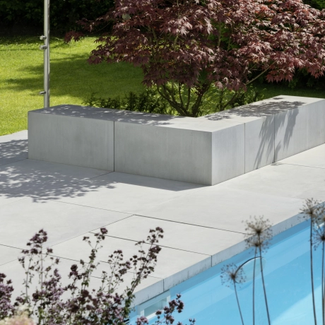 Sitzfläche, Sitzbänke aus Beton in Sichtbeton umranden einen roten Baum neben einem pool