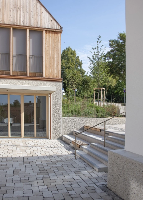 Modern building with upper wooden façade, large windows and ecologically paved inner courtyard with stairs.
