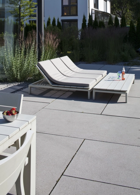 niedriger breiter Liegestuhl auf Terrasse mit großformatigen grauen Terrassenplatten